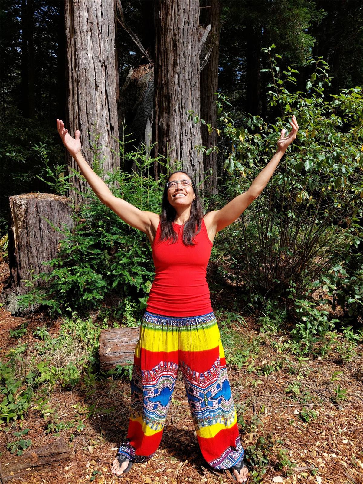 Gigi with arms raised among redwood trees